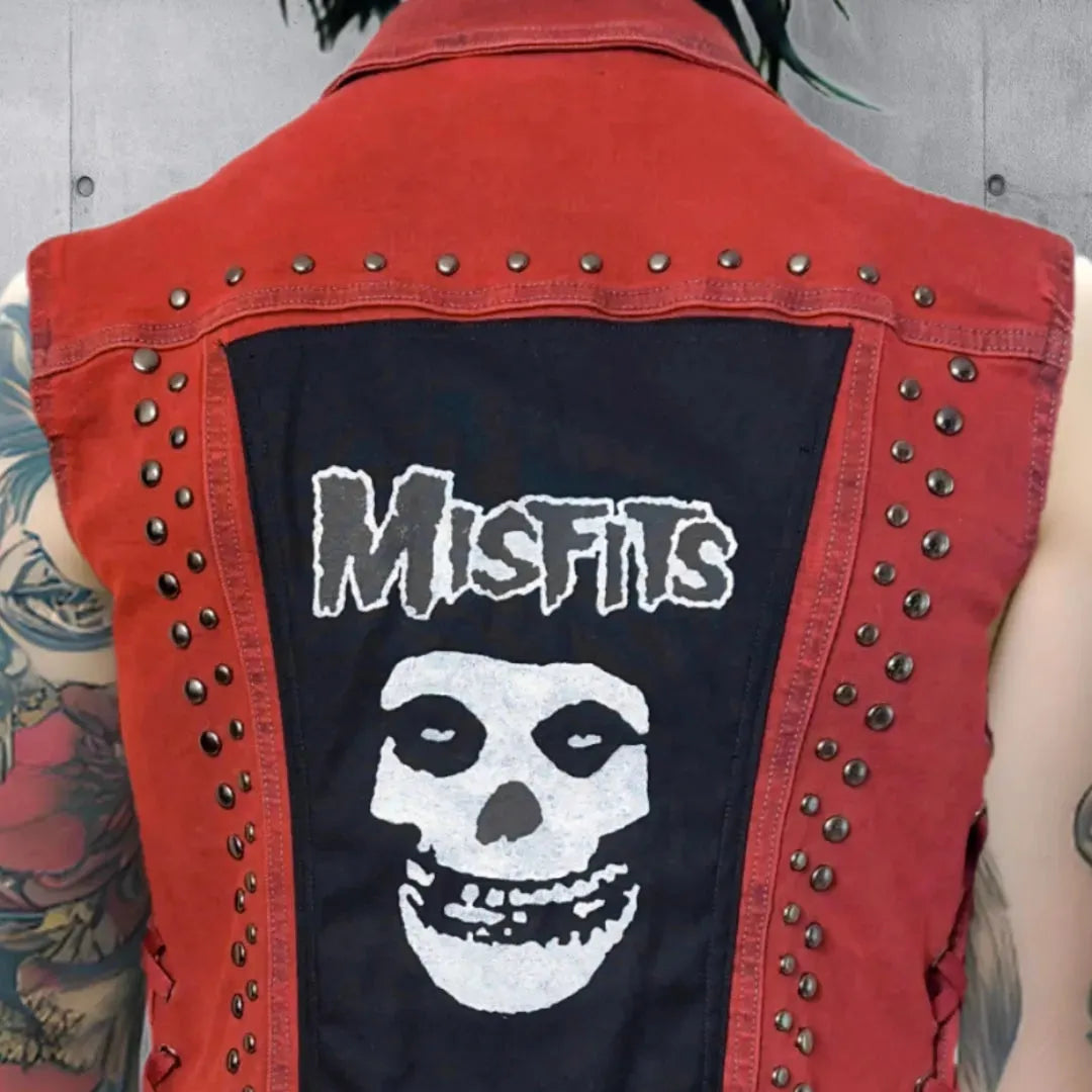 Upper view close up of a red vest with Misfits skull patch and gunmetal colored round punk studs, showing detailed arm tattoos.