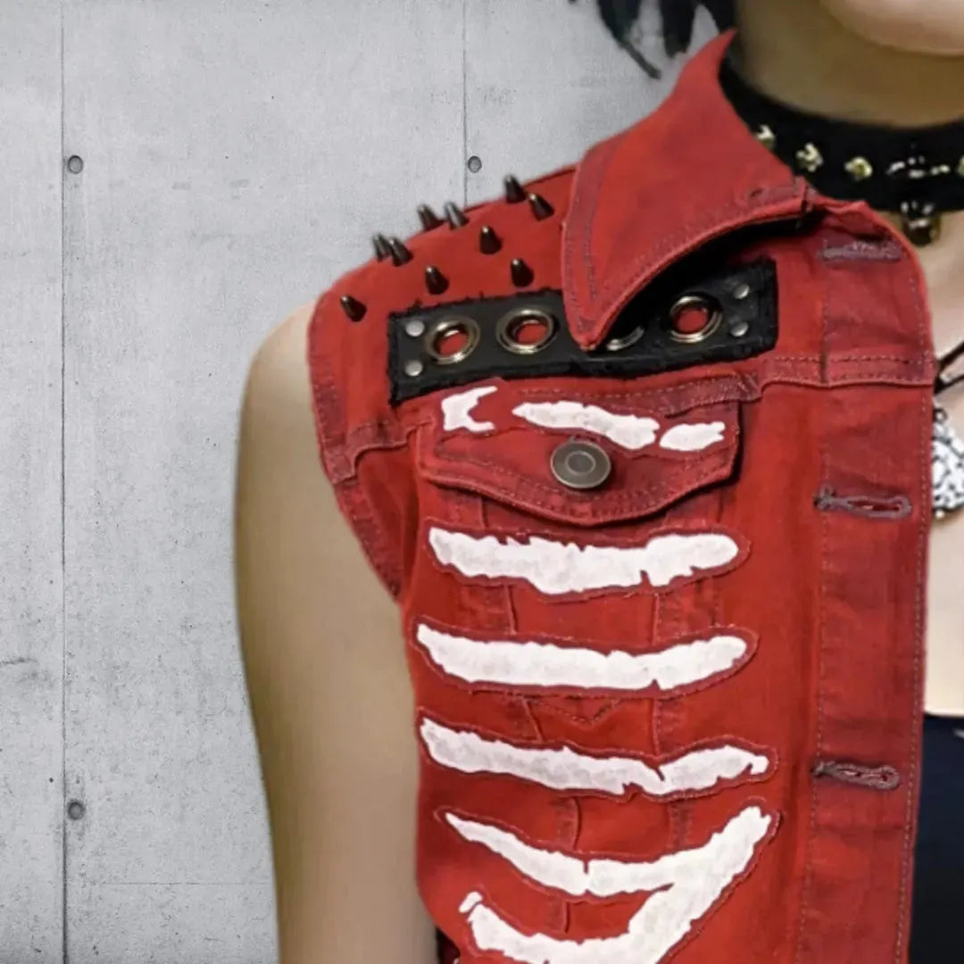 Close up, upper right side view of a red vest with white skeleton rib cage patches, gunmetal colored studs,and button details, worn by a woman with black hair and a studded choker.