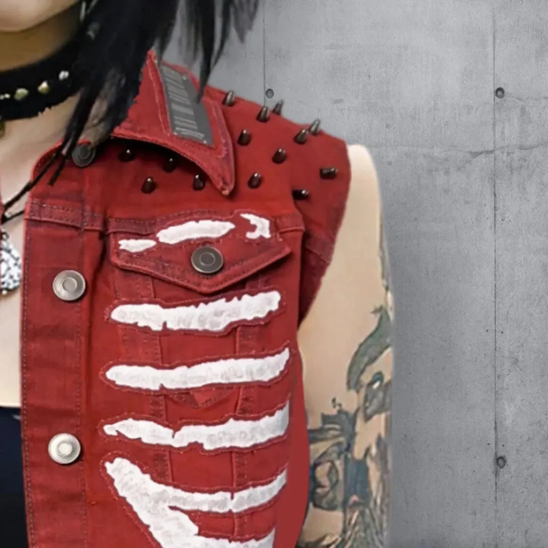 Close up, upper left side view of a red vest with white skeleton rib cage patches, gunmetal colored studs,and button details, worn by a woman with black hair and a studded choker.