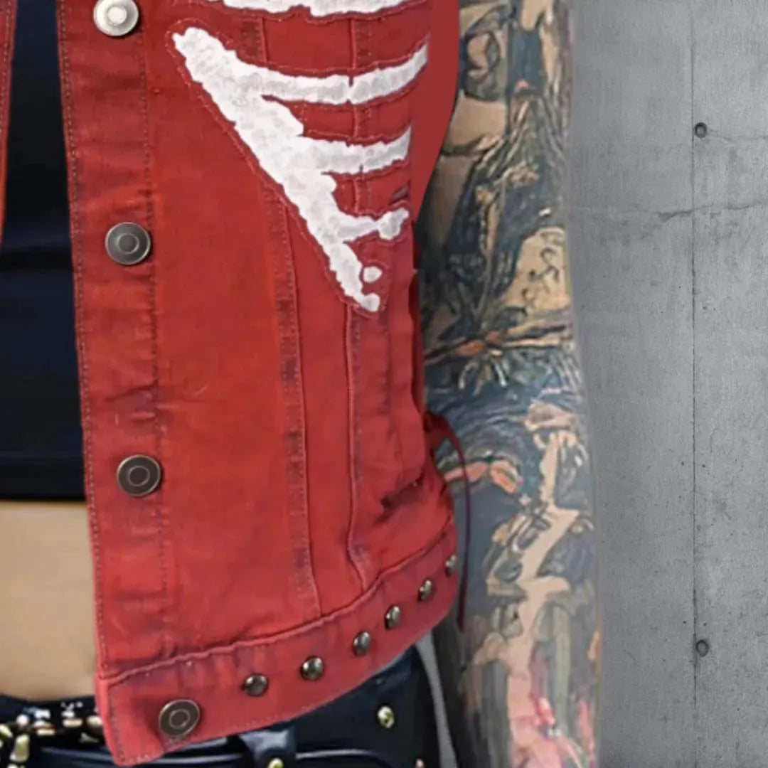 Lower left side detail of a red vest with white skeleton rib cage patches, the jacket hem lined with gunmetal round punk studs, worn over a black crop top and red plaid mini skirt.