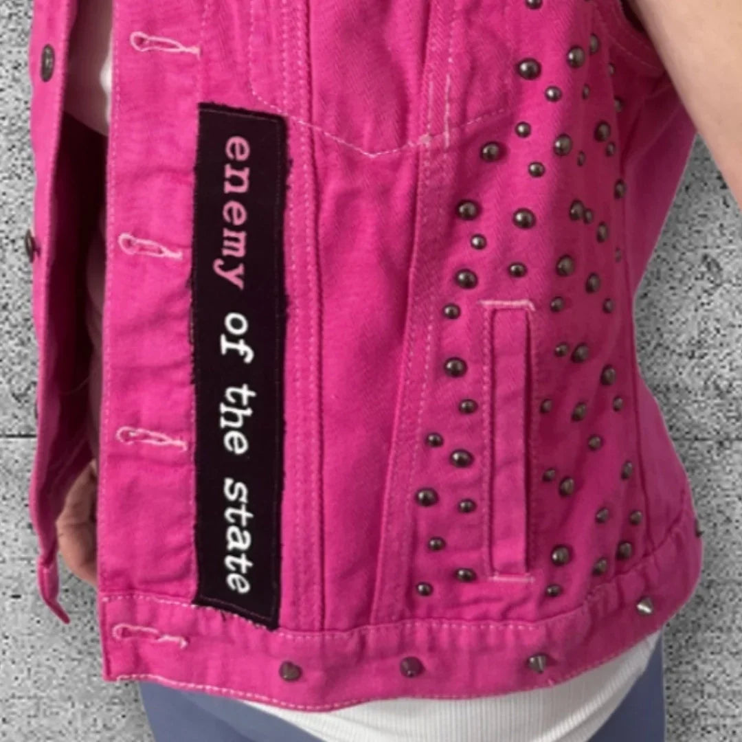 Women's pink punk vest with metal studs and 'enemy of the state' patch