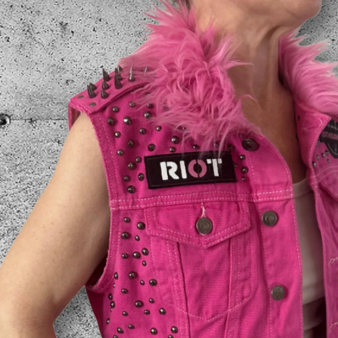 Pink studded punk vest with 'RIOT' patch and feather collar, edgy rocker fashion for bold style