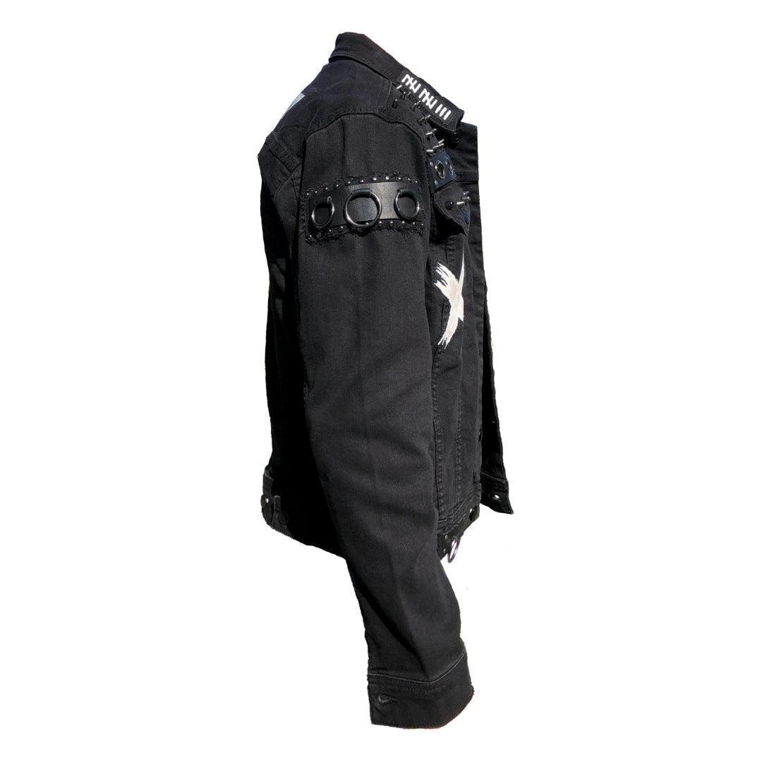 Right side view of a black denim punk-inspired jacket featuring black leather studded accent patch with metal o rings attached on right side arm.