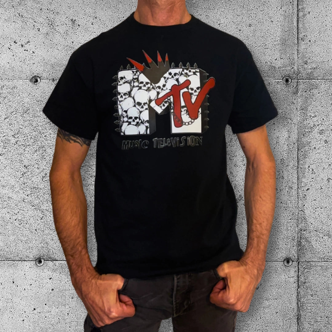 Man wearing black punk MTV T-shirt with skull graphic, rocker clothing against concrete wall